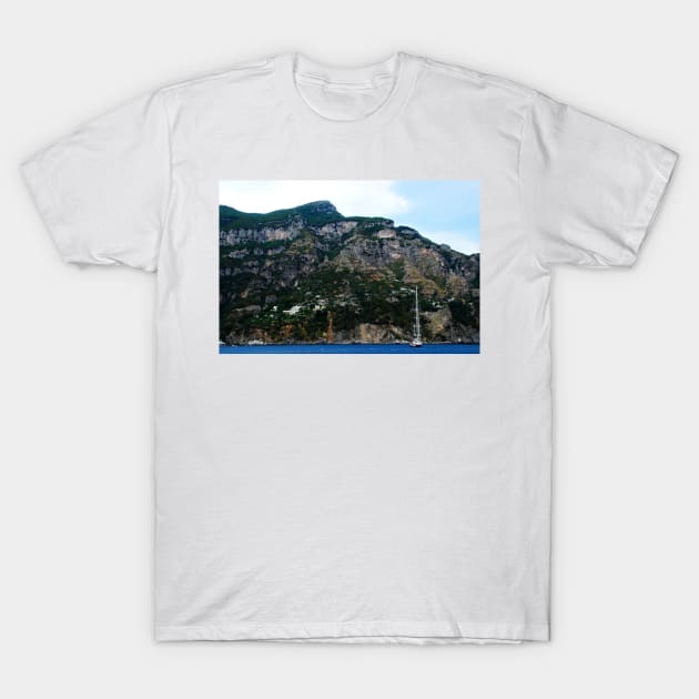 View in Amalfi coast at a huge mountain with rocky parts, greenery and buildings with a white boat underneath T-Shirt by KristinaDrozd